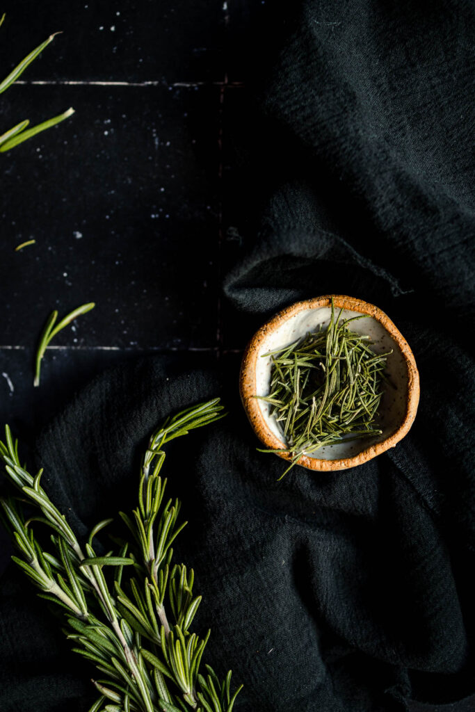 Rosemary sprigs in a bowl on a black cloth.
