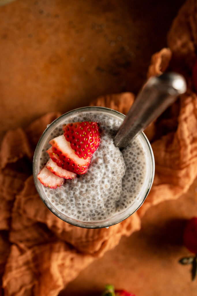 A glass of chia pudding with strawberries and a spoon.