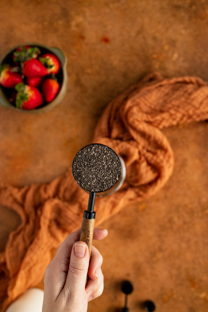 A person is holding a chia seed grinder in front of strawberries.