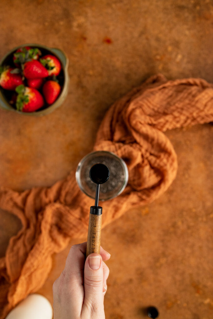 A person holding a wooden spoon in front of strawberries.