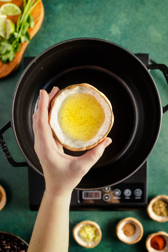 A person is holding a bowl of oil in front of a pan.