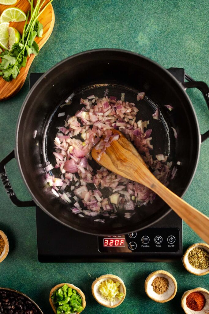 A pan with onions and a wooden spoon.