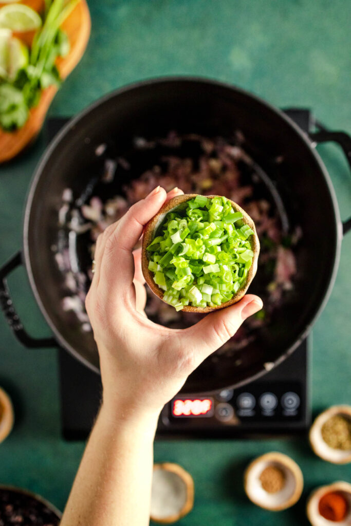 A hand holding a bowl of green onions on a stovetop.