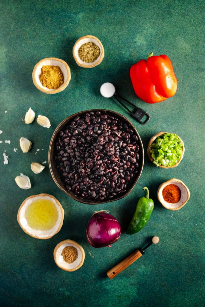 A bowl of black beans, peppers and other ingredients on a green background.