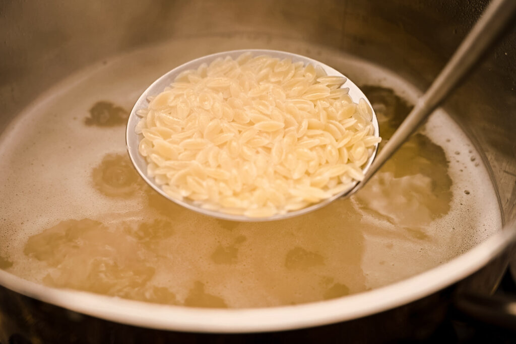 A spoon of pasta in a pot of liquid.