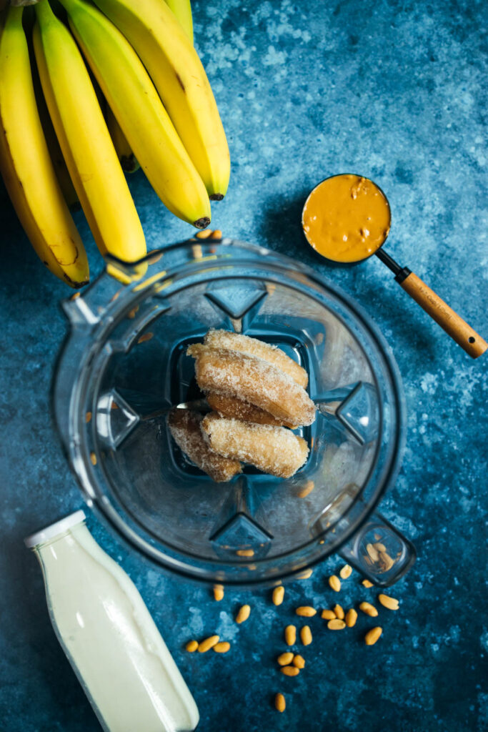 Bananas and peanut butter in a blender on a blue background.