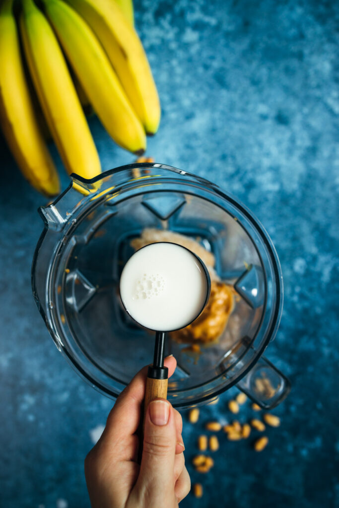 A person holding a blender with milk and bananas.