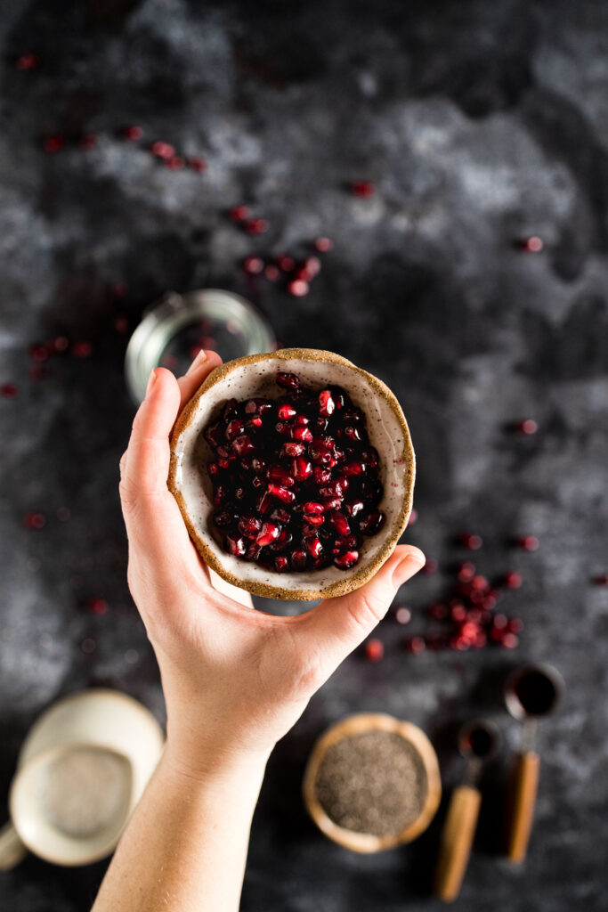 A hand holding a bowl of pomegranate seeds.