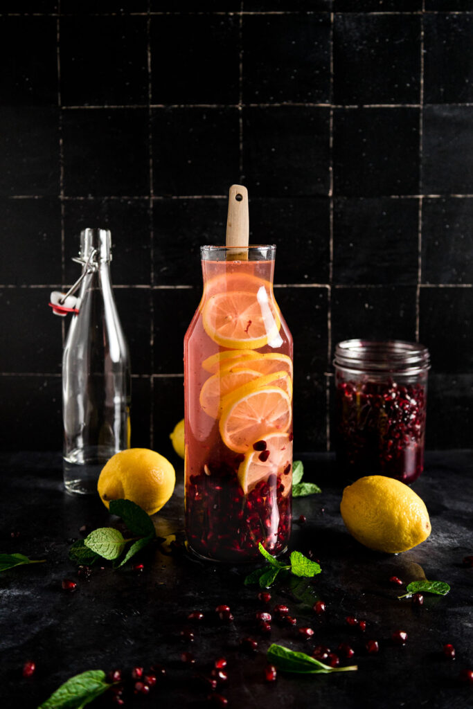 A glass of pomegranate juice with lemon slices and mint leaves.