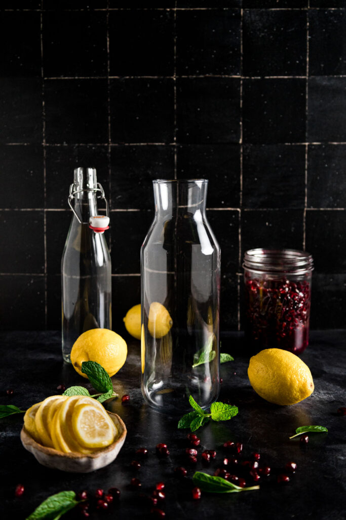 A glass jar with lemons and pomegranates on a black background.