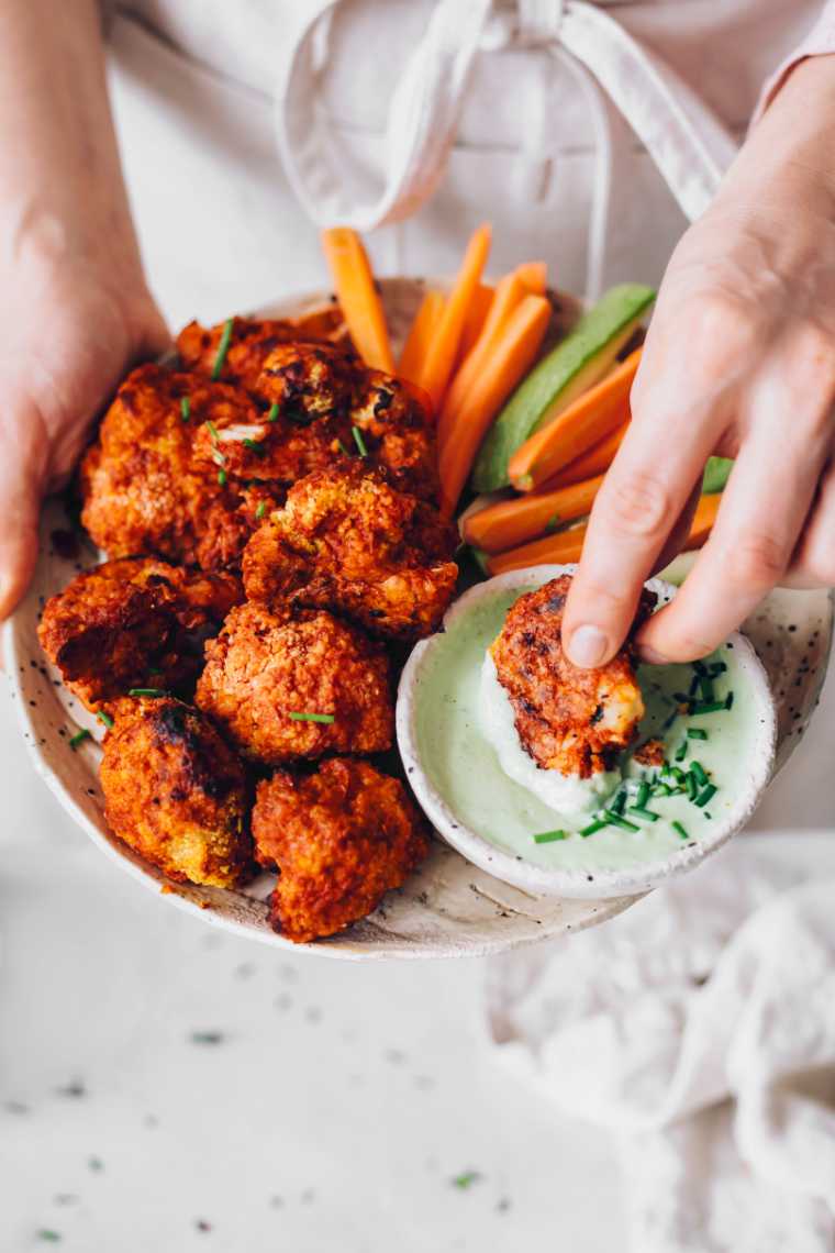 A person holding a plate of cauliflower wings with dipping sauce, perfect for game day or Super Bowl recipes.