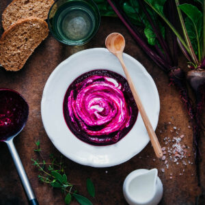 A bowl of beetroot soup with bread on a wooden table.