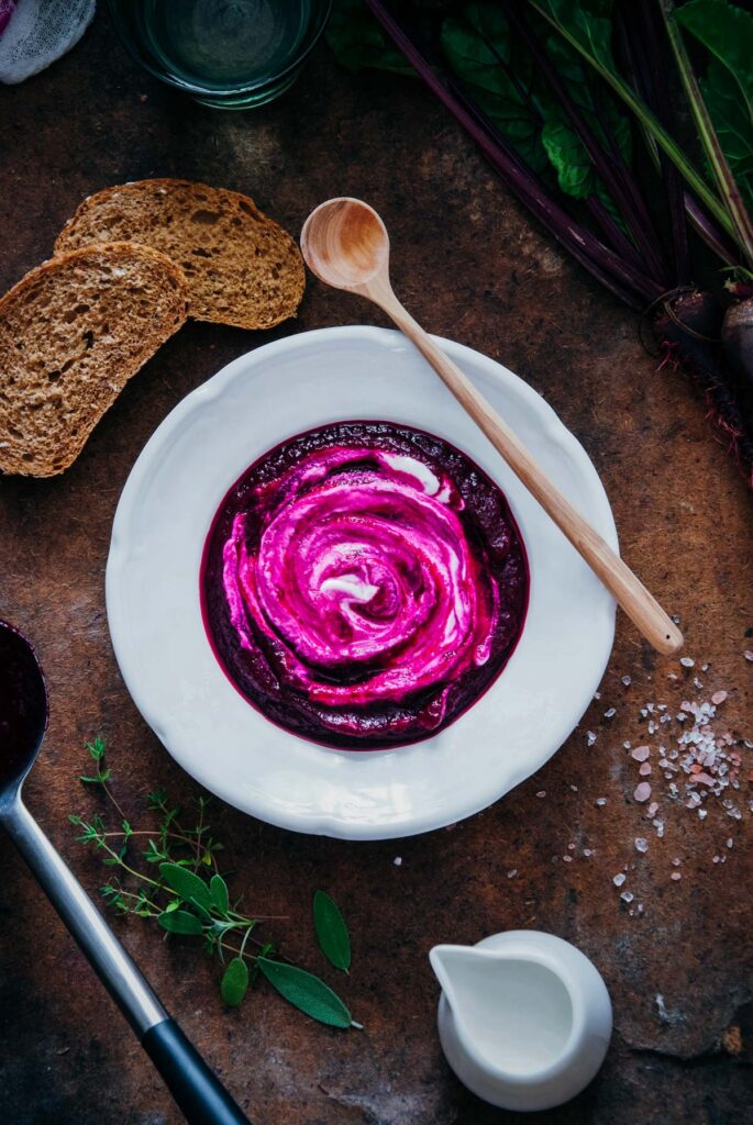 A bowl of beetroot soup with bread and a spoon.