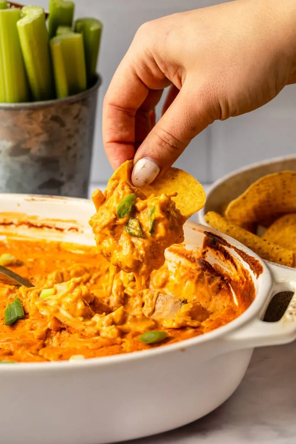 A hand dipping into a bowl of buffalo chicken dip, perfect for Super Bowl gatherings and game day recipes.