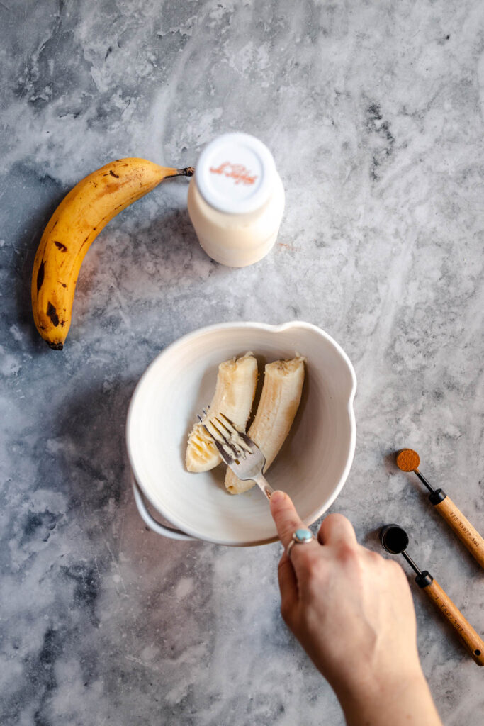 Preparing a banana snack with sliced banana on a plate, a bottle of milk, and utensils on a marble surface.