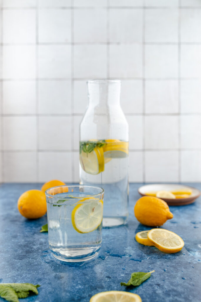 A refreshing setup of lemon-infused water with a glass bottle, a drinking glass, and fresh lemons on a blue surface.