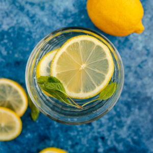 A glass of lemon water with mint leaves on a blue background.