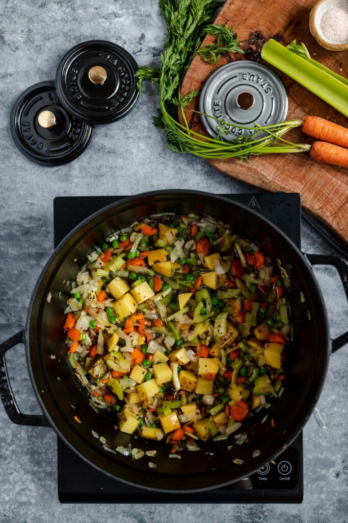 A variety of chopped vegetables cooking in a pot on an induction stove.