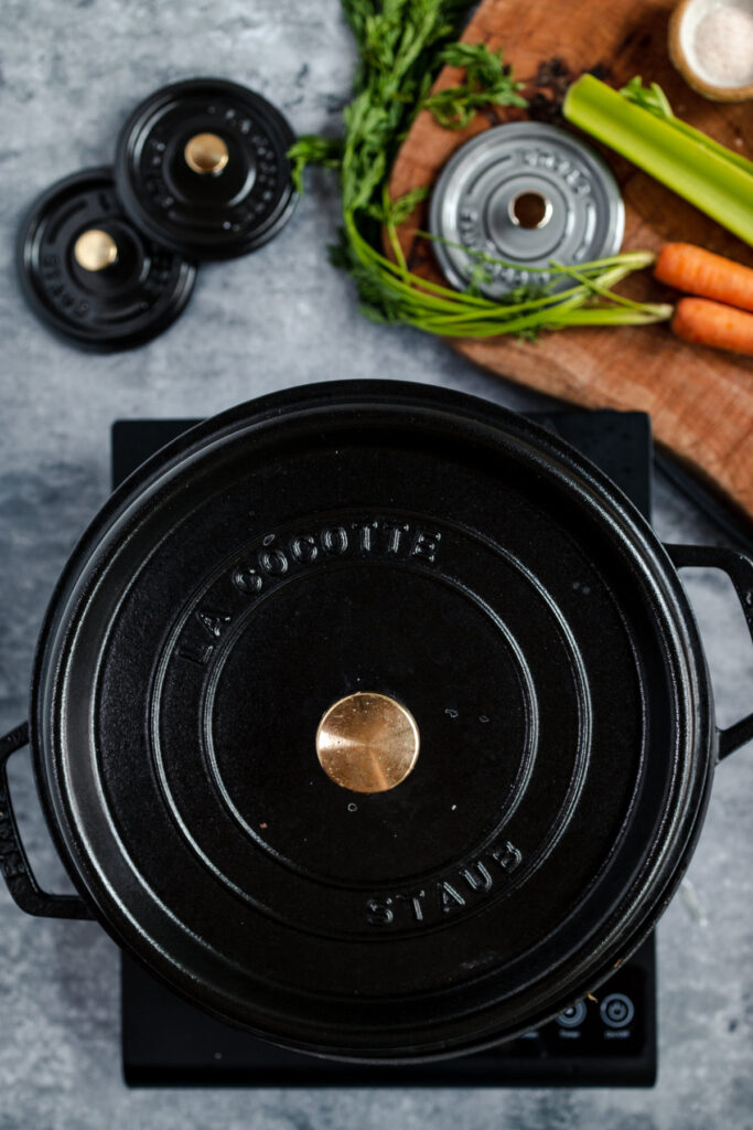 Black cast iron pot on a stove with fresh vegetables nearby.