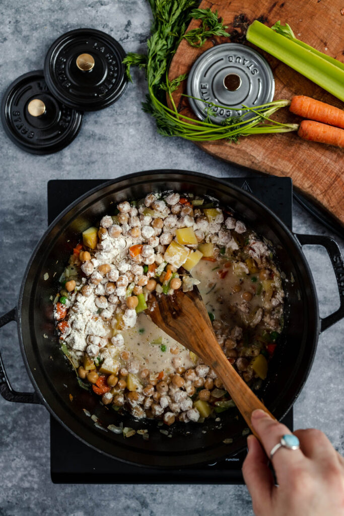Stirring a hearty vegetable and ground meat stew in a black skillet on a stove top.
