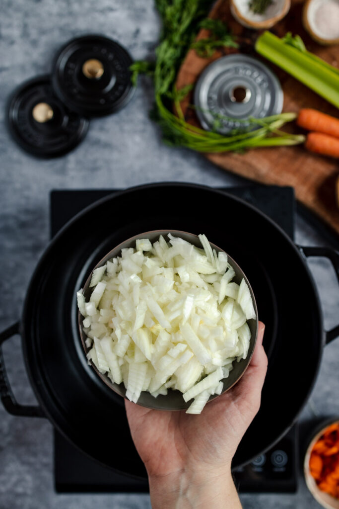 Chopped onions being added to a pot on a stove with ingredients in the background.