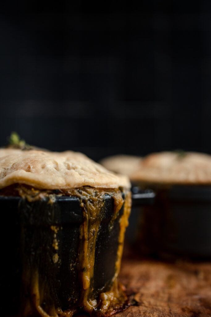 Savory pot pies with overflowing filling on a wooden surface.