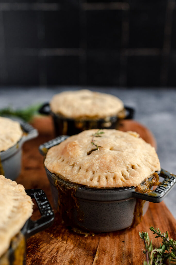 Freshly baked individual pot pies with a golden crust, garnished with herbs, served in black ramekins on a wooden board.
