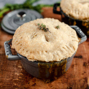 Individual pot pie with golden crust in a mini casserole dish on a wooden surface.