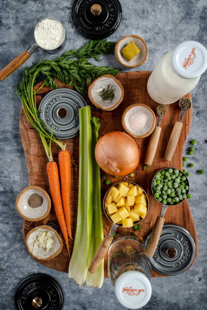 An assortment of fresh vegetables, herbs, and spices neatly arranged on a wooden board, ready for cooking.