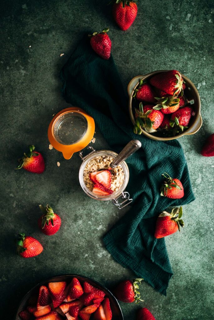 Overhead view of a healthy breakfast setup with oats and strawberries on a textured green surface.