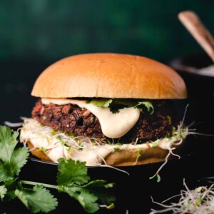 A gourmet burger with a thick patty, topped with cheese, sprouts, and cilantro, served in a brioche bun.