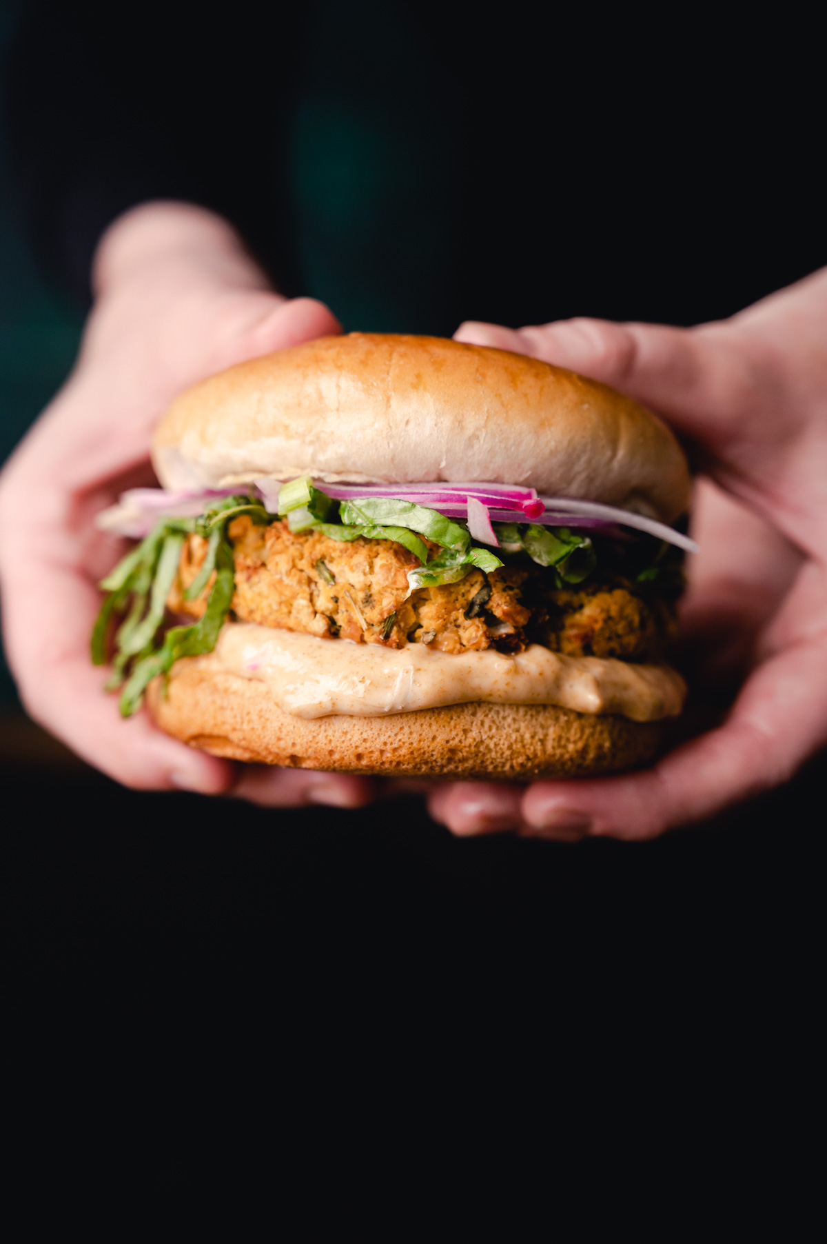 Hands holding a crispy chicken sandwich with lettuce, red onions, and a light sauce on a bun.