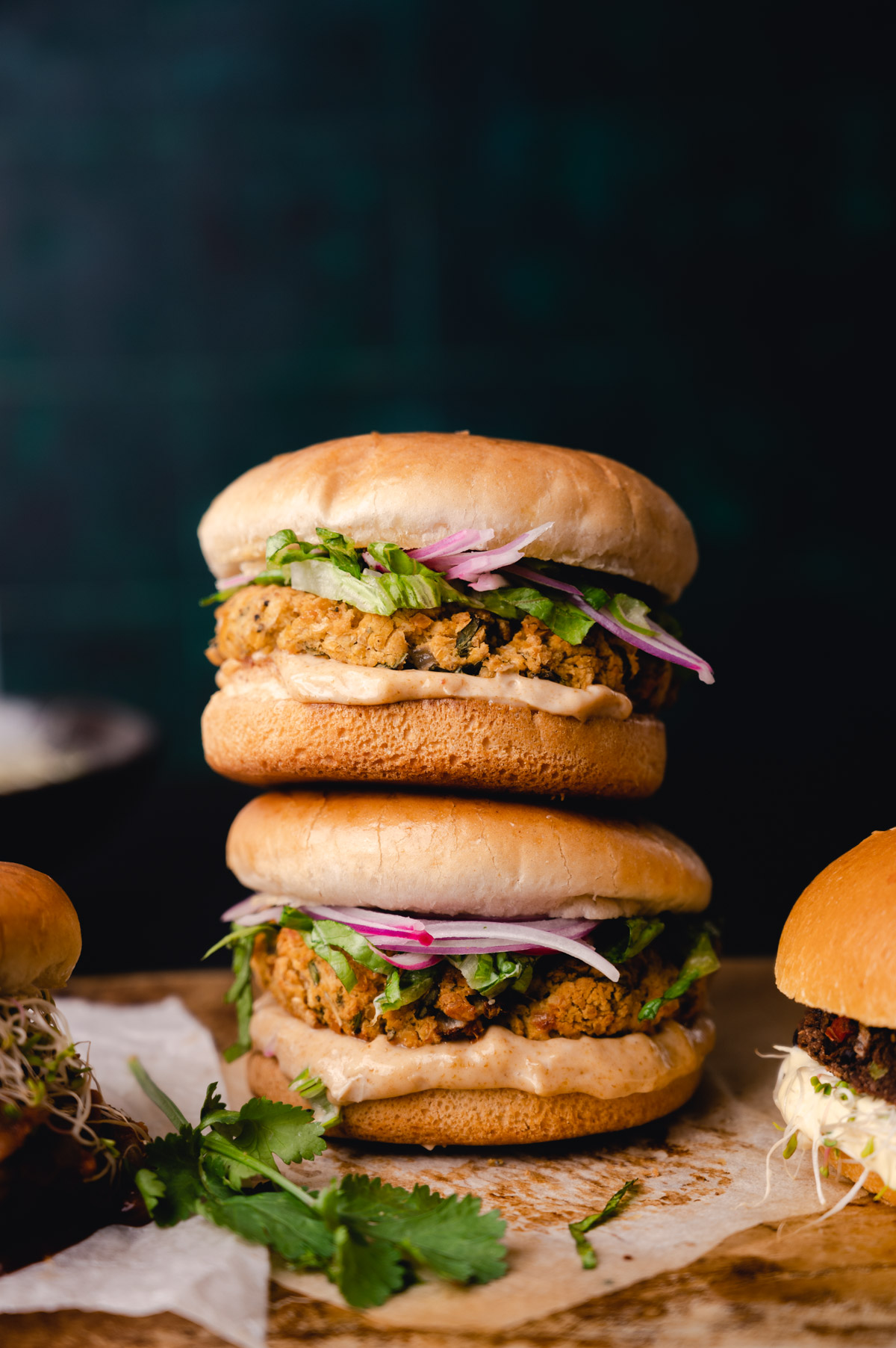 Three stacked chicken sandwiches with pickled red onions and cilantro, served on a rustic wooden surface.