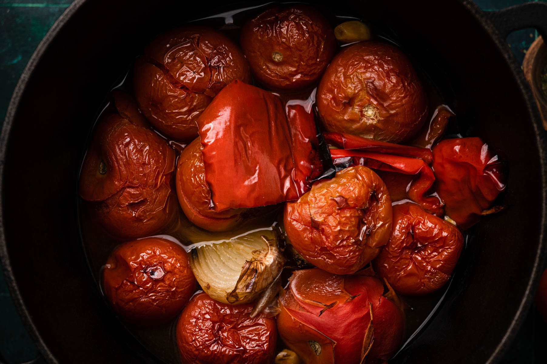 Roasted tomatoes and red peppers in a bowl, with a halved onion visible, all glistening with cooking juices.