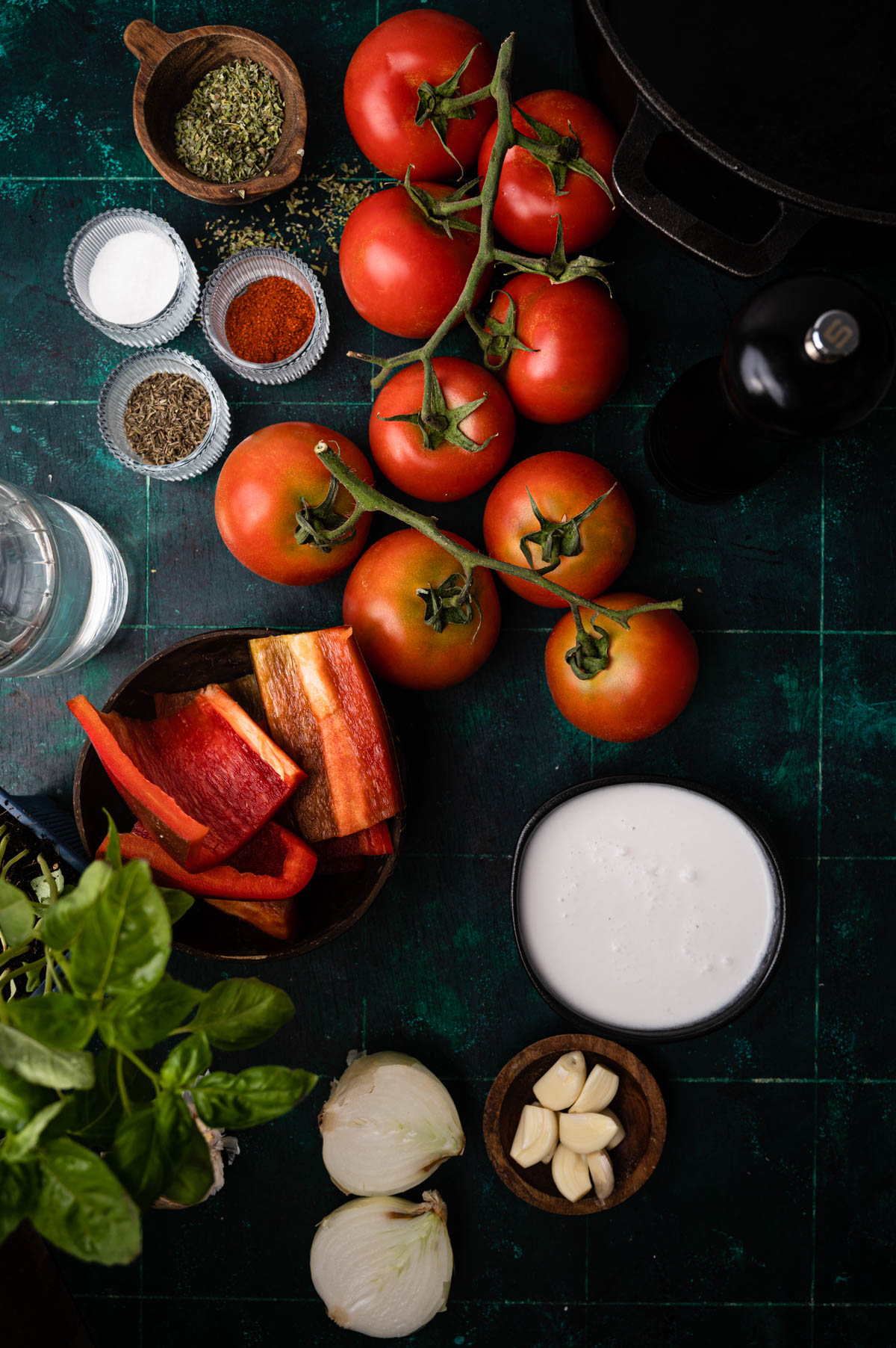 Top view of a kitchen counter with fresh tomatoes, spices, sliced bell peppers, onions, garlic, and a bowl of sauce, arranged neatly for cooking.