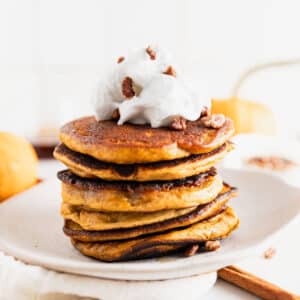 Tall stack of pumpkin spice pancakes with vegan whipped cream on top.
