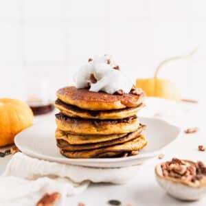 Tall stack of pumpkin spice pancakes with vegan whipped cream on top.