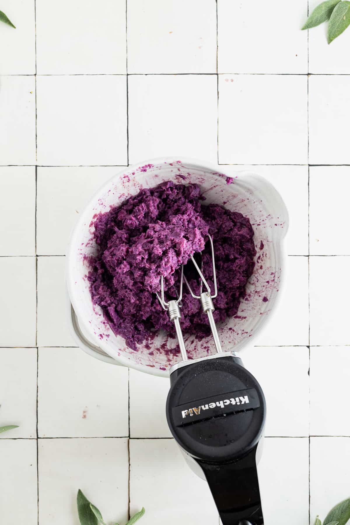 Using a hand mixer to whip and mix the sweet potato casserole ingredients.