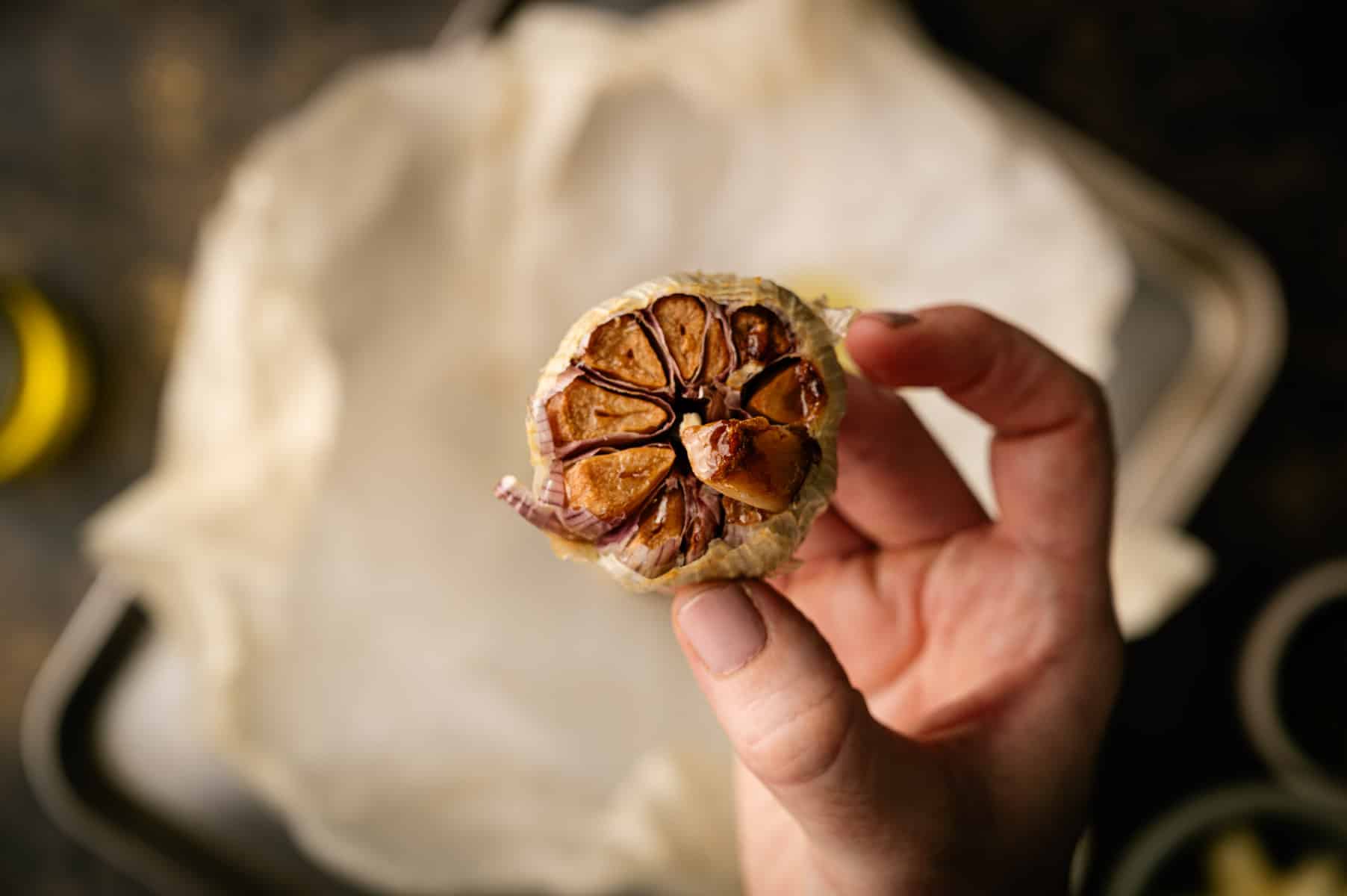 Woman holding roasted garlic bulb over parchment paper.