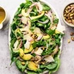 Arugula and spinach salad with sliced avocado, onion, pistachios, and shaved vegan Parmesan.
