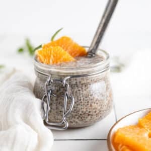 Homemade chia seed pudding with ground flax in a glass jar and orange slices and herbs on top.