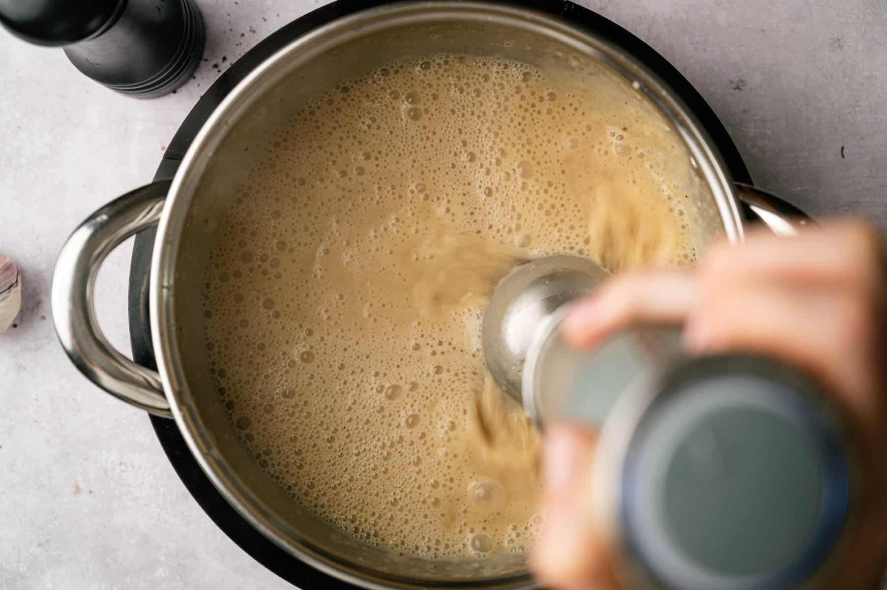 Immersion blender going into the soup pot blending the ingredients together.