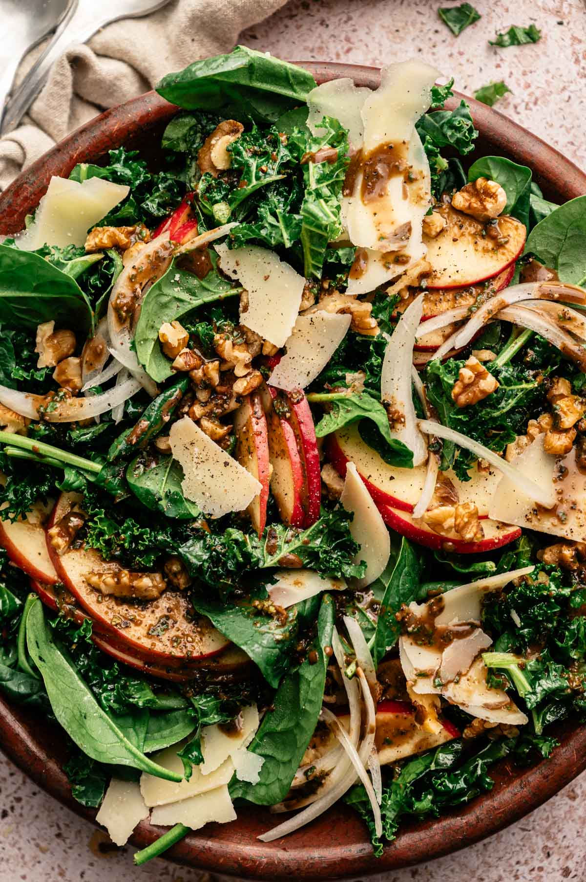 Close up of green salad recipe with sliced onion, apples, walnuts, vegan parmesan, and homemade basil balsamic dressing.