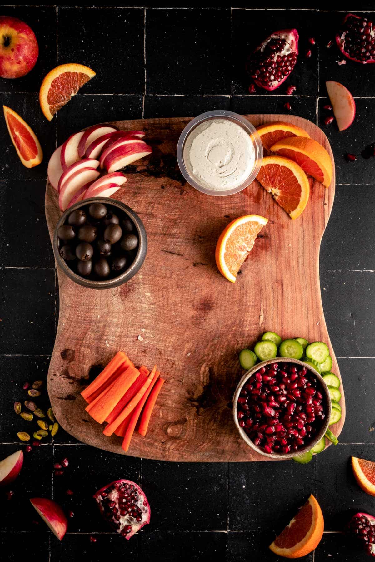 Fruit and veggies on the wooden board surrounding the larger round items.