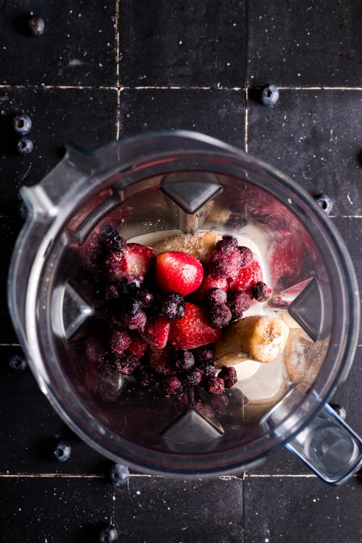 Frozen fruit and milk in a blender pitcher.