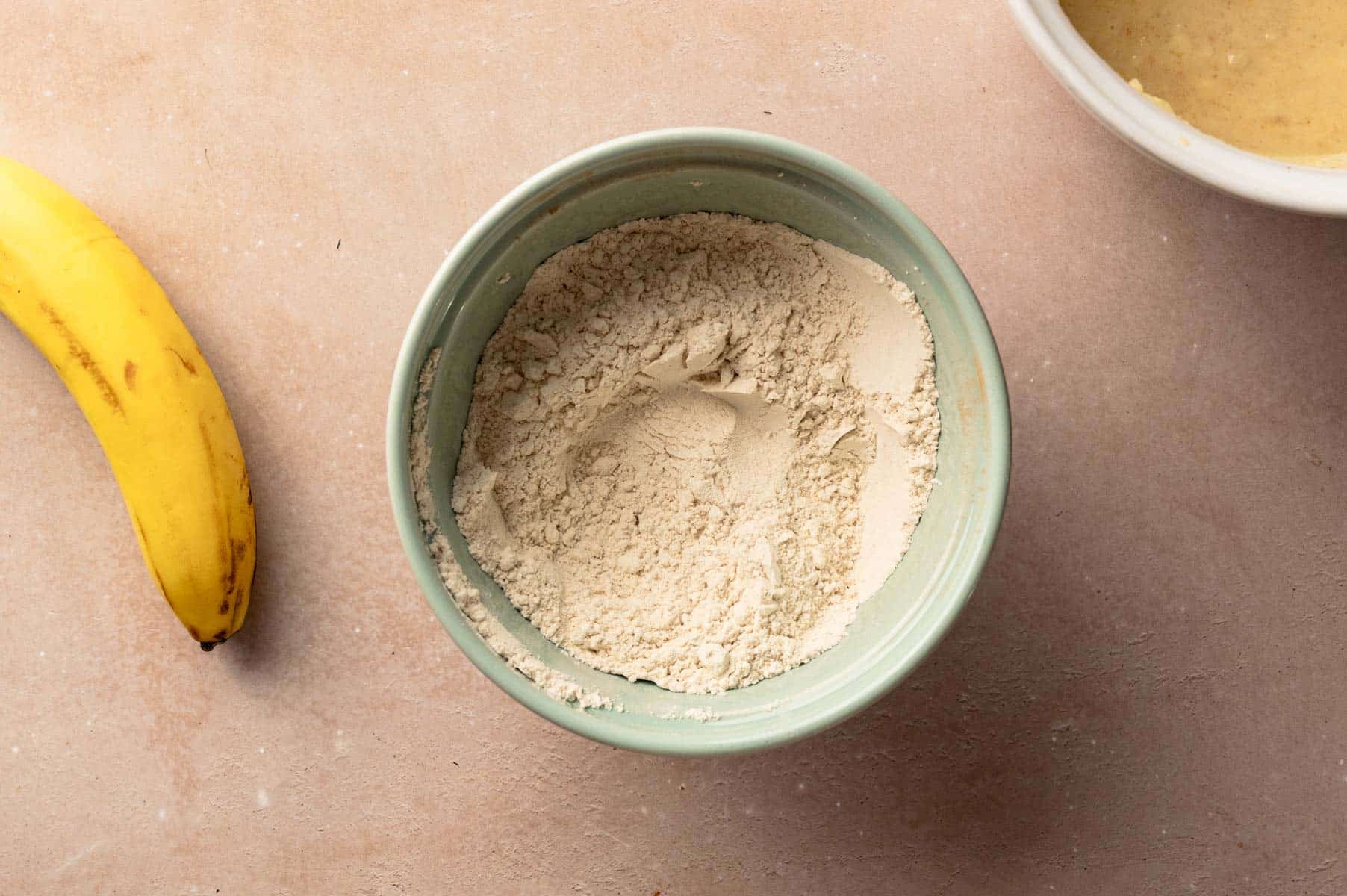Dry ingredients for homemade high protein muffins in a sea green mixing bowl mixed together.
