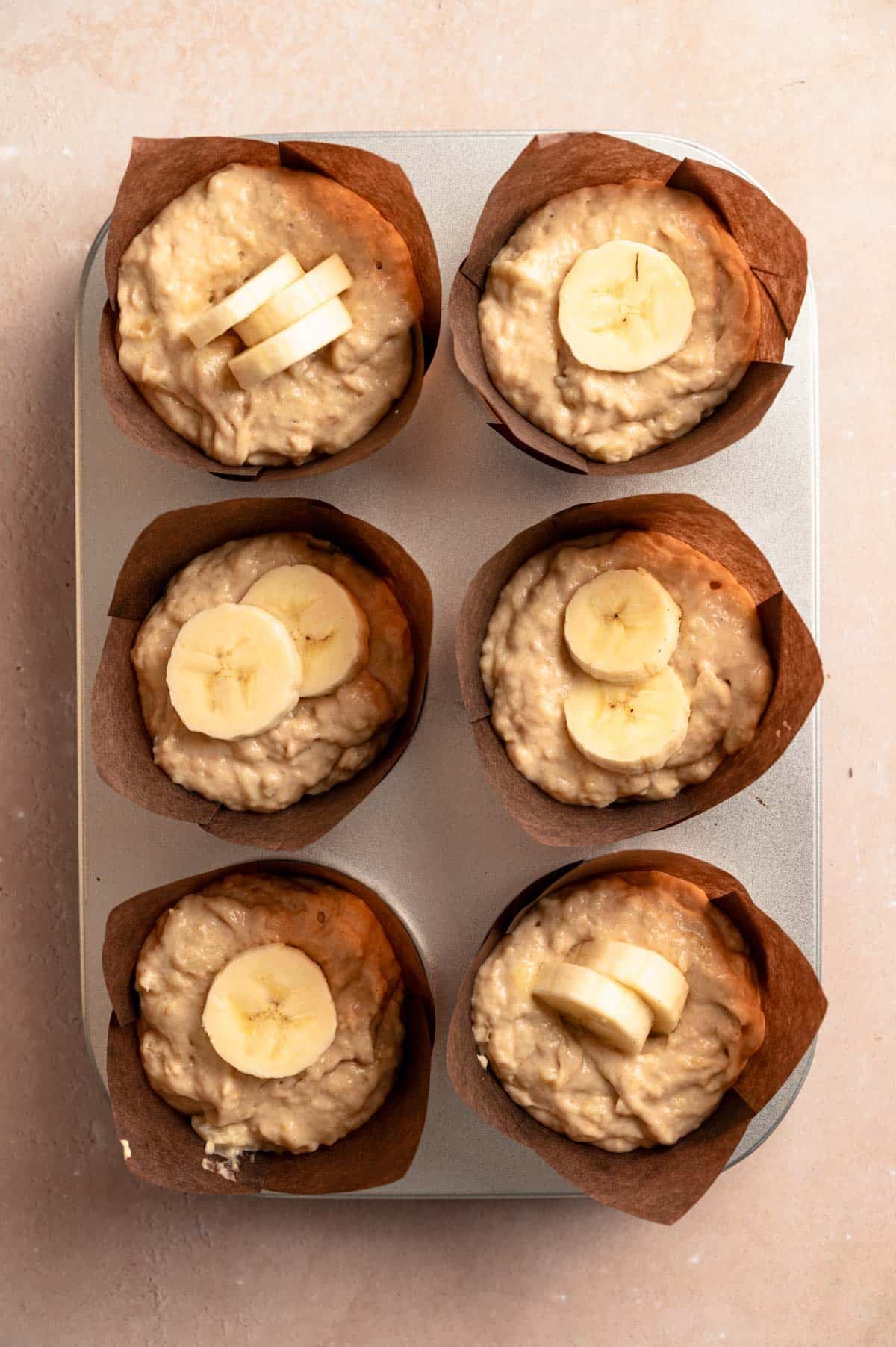 Vegan banana protein muffins in a muffin tin with banana slices on top.