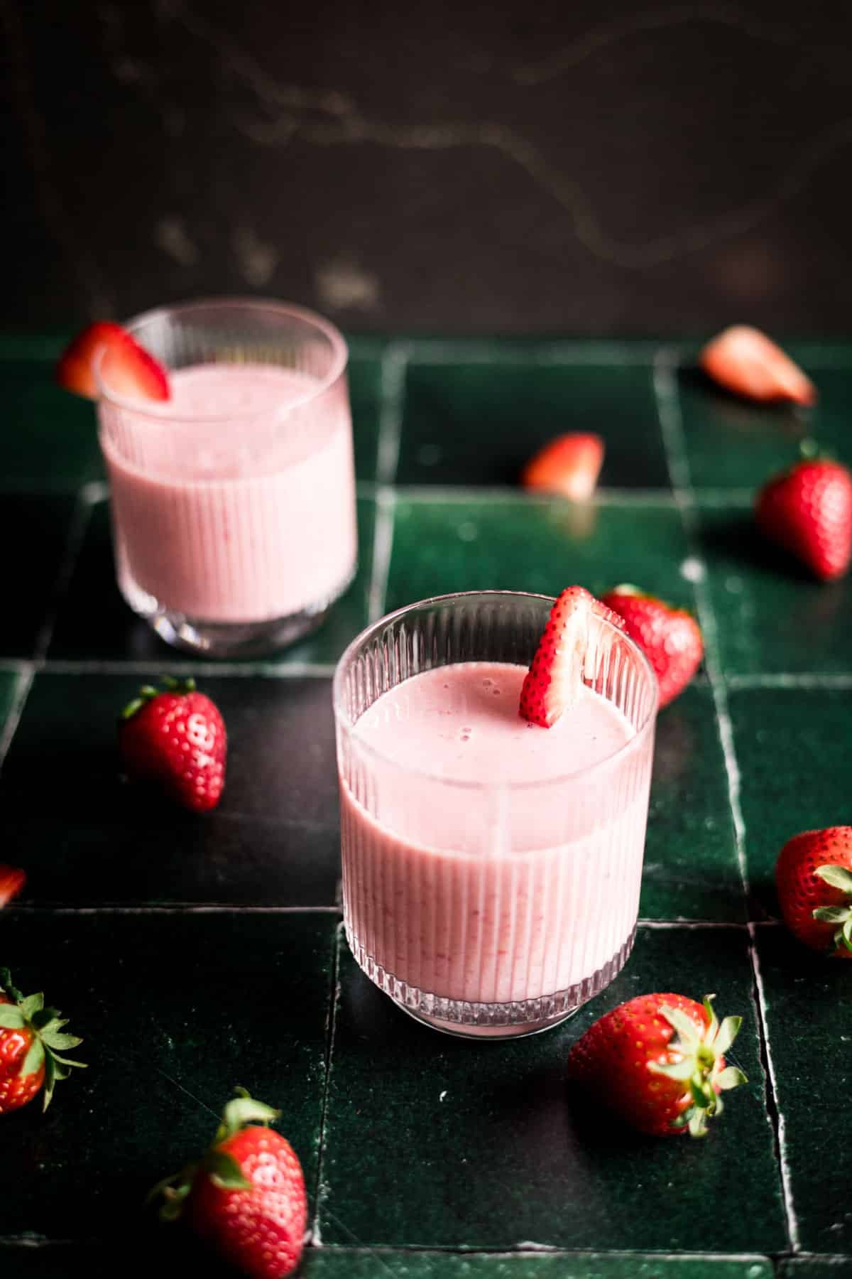 Fresh strawberry and banana smoothie in glass cups with strawberry slice on the rim.