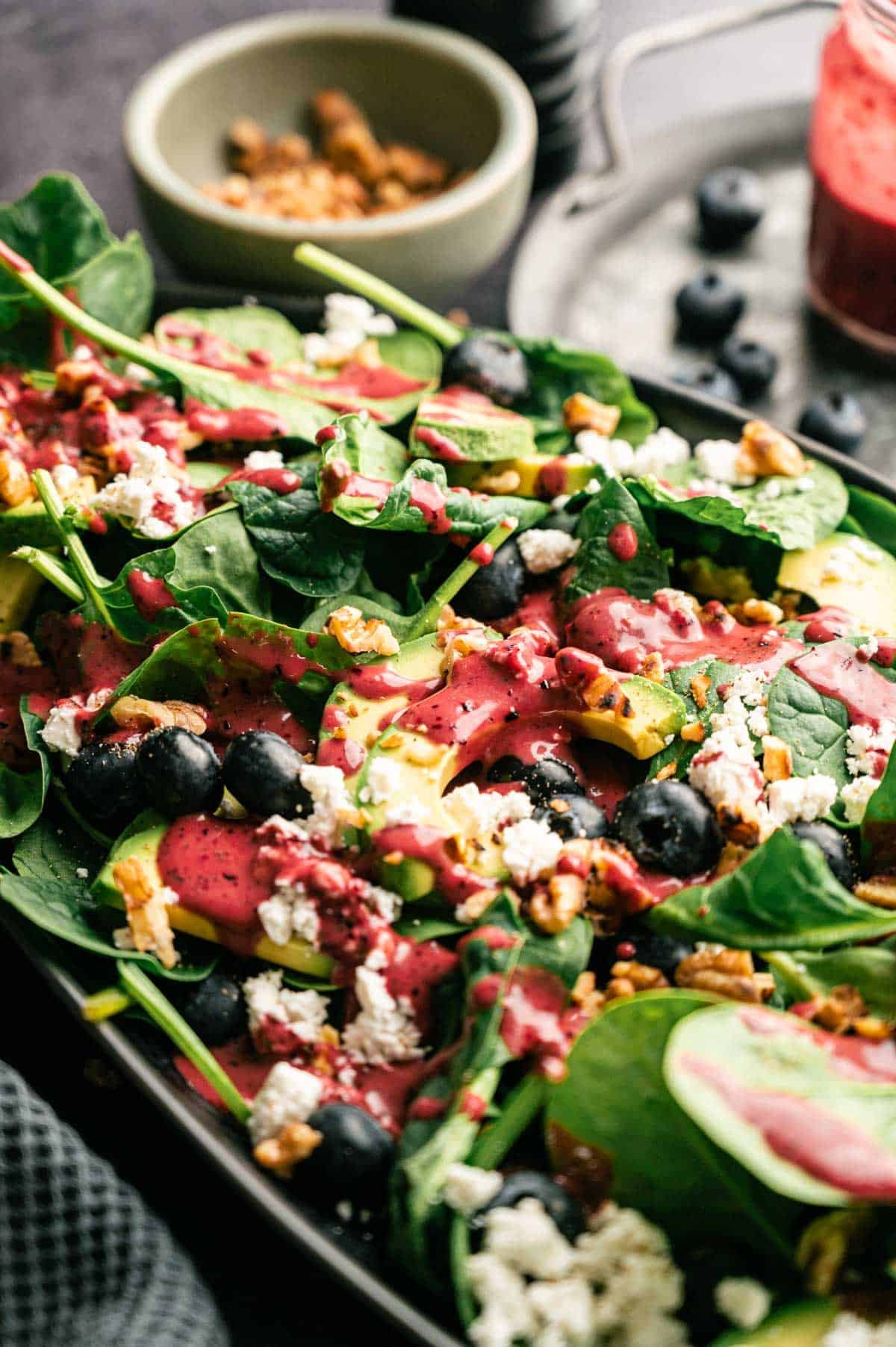 Blueberry dressing being poured over spinach and blueberry salad.