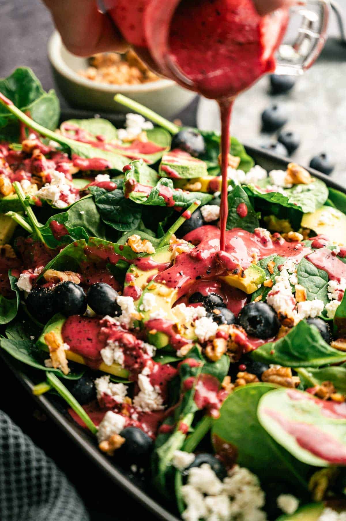 Blueberry dressing being poured over spinach and blueberry salad.